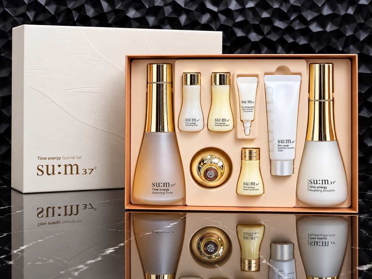 A su:m37 Time energy Special Set skincare gift set, featuring multiple cream and serum bottles with gold caps arranged in an open peach-colored box next to its white outer packaging box, set against a dark textured background.